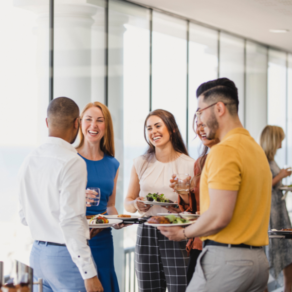 A group of corporate staff socially interacting and smiling while holding plates with food.